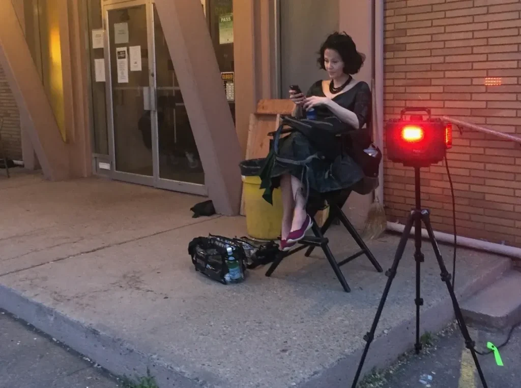 PortaBell wireless bell and light system operating outside a film set location, signaling ‘rolling’ while a hair and makeup crew member sits nearby between takes.